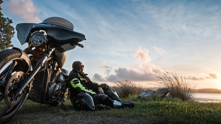 Motorcyclists sits on grass, leaning against his bike.