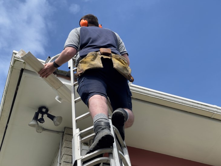 A man on a ladder fixing the guttering on a house. 