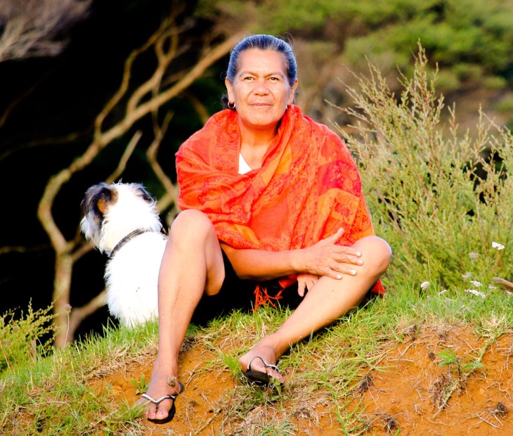 Rongoā Māori practitioner Atarangi Muru sitting on a grassy bank with a dog in the background.