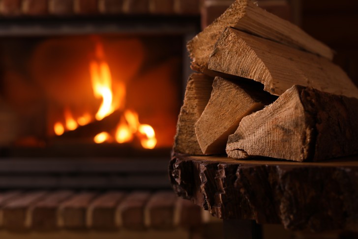 A pile of firewood in a basket in front of a fireplace.