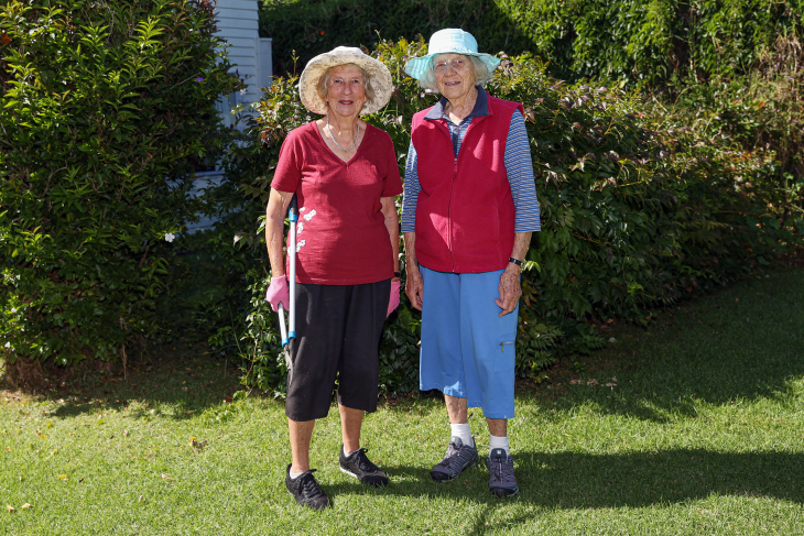 Penny Wilson standing in the garden with her friend, both are smiling and looking towards the camera.