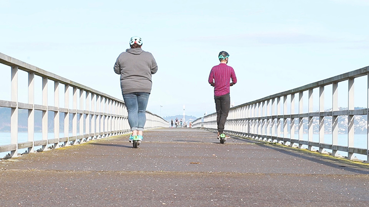 Two people scoot along Petone Wharf on e-scooters