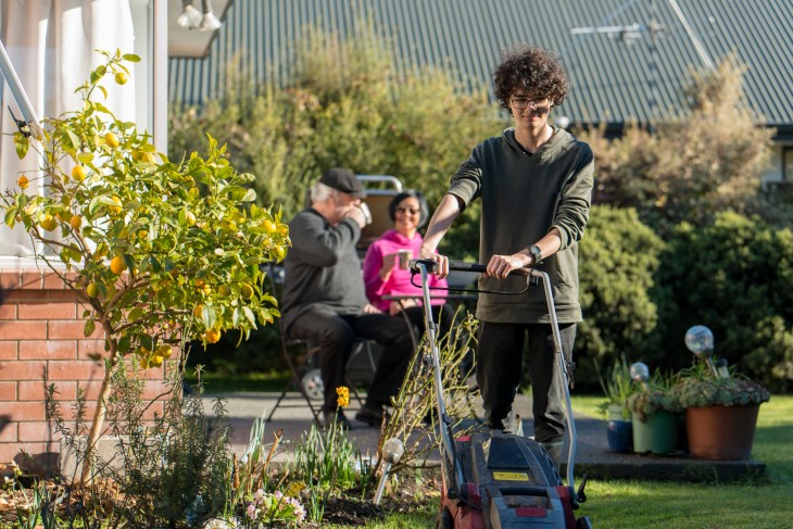Young man mows lawn for older couple