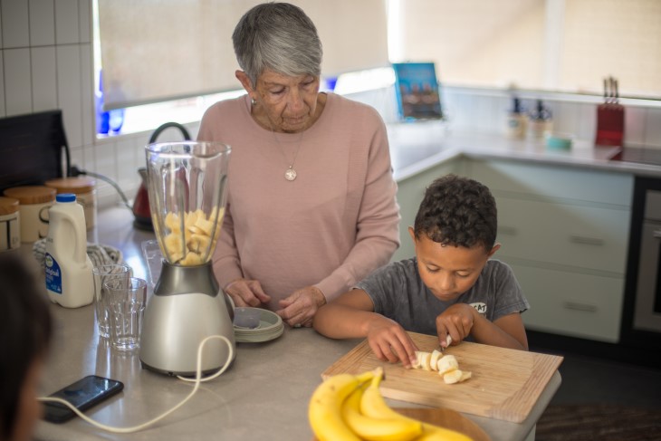 Child cuts banana while grandma watches