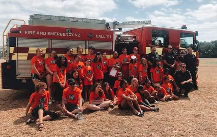 Brayden and a group of kids pose with a fire truck and some fire officers