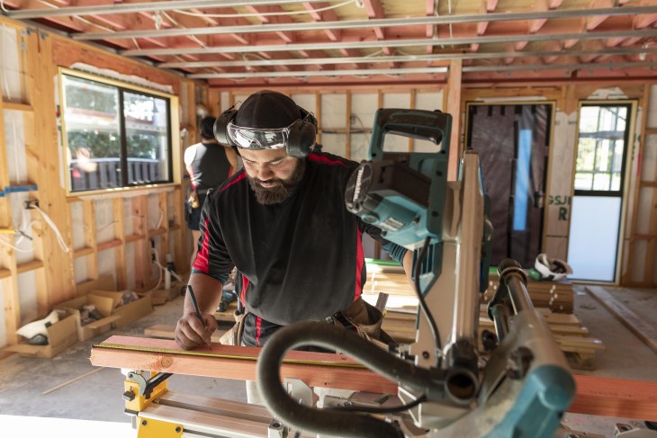 Building worker measures a cut before sawing