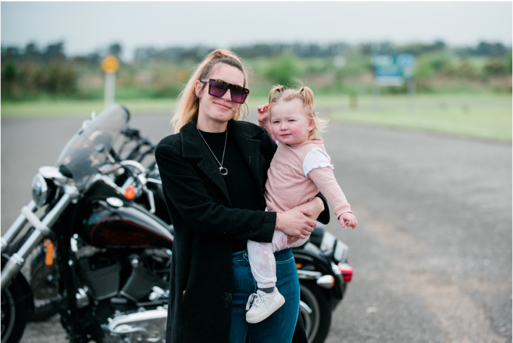 Kavana Jane holds daughter Harley by a Harley Davidson motorcycle