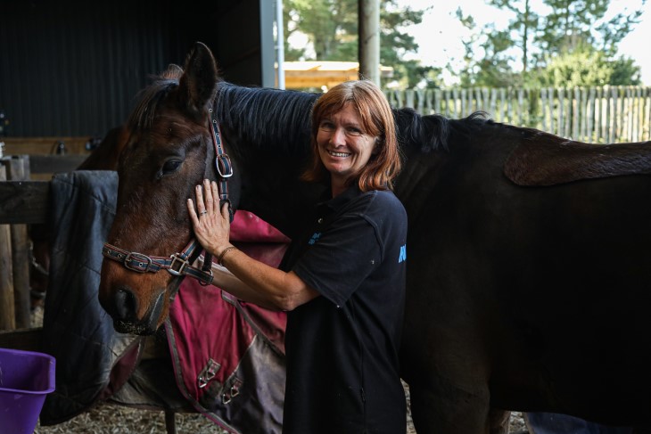 Lenka rubs her horse's face while looking into the camera