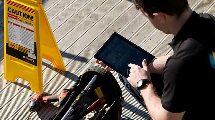 Man kneeling over tool bag and using tablet