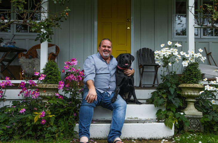 Martin sits with his black lab on the steps of his cottage