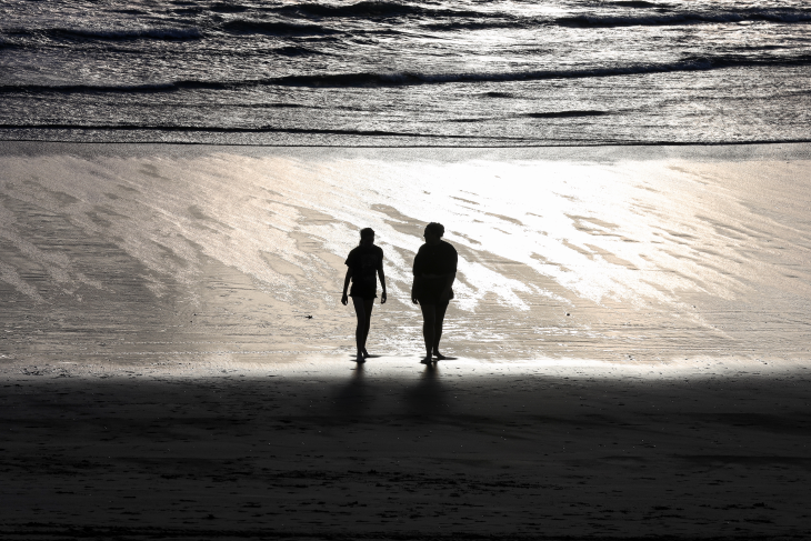 Paris and Maddison walk along the shore at Muriwai