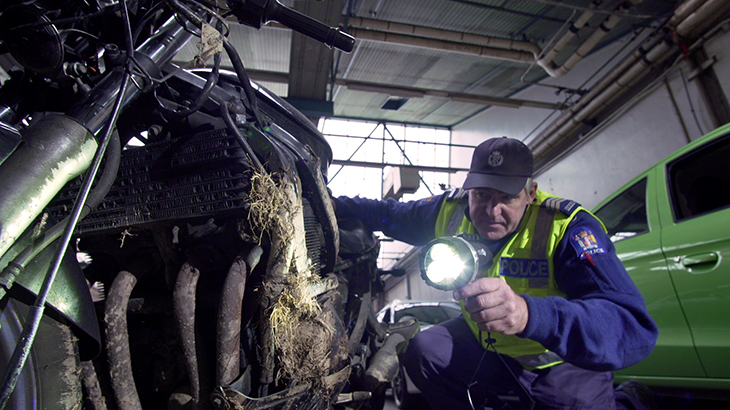 Peter Sowter crouches down, aiming a light at a muddy motorbike