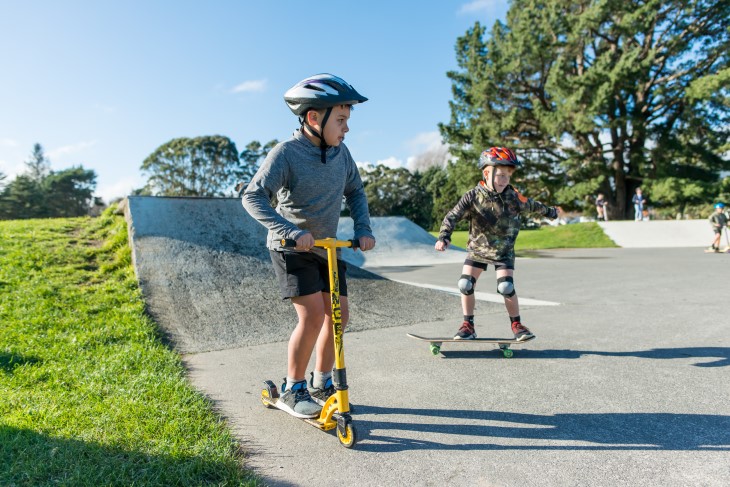 Young children ride scooters at a skate park