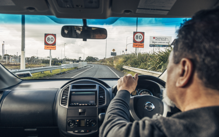 Camera looks over a drivers shoulder through the windscreen as they drive onto a highway