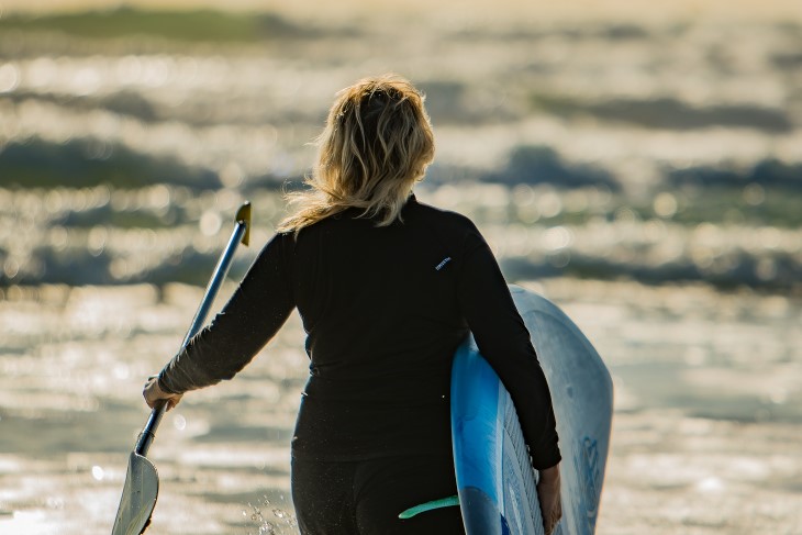 Verity walks towards the sea holding her paddleboard