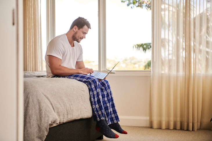 Man works on the bed in his pyjamas