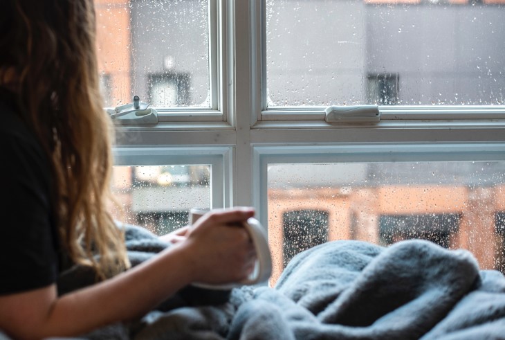 Person drinking tea in bed looks out of a condensated window