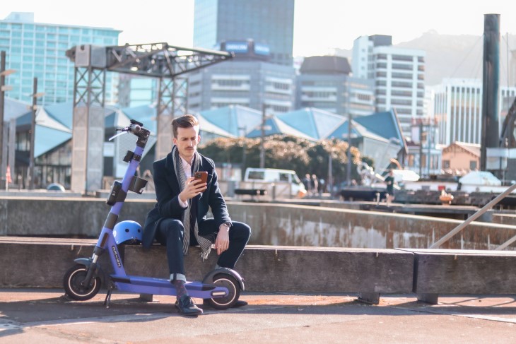 Guy reads phone beside an e-scooter