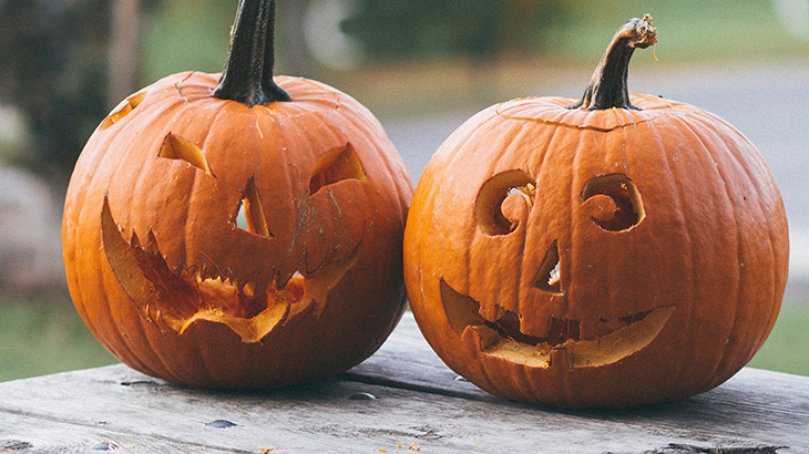 Two carved pumpkins sitting on a wooden table