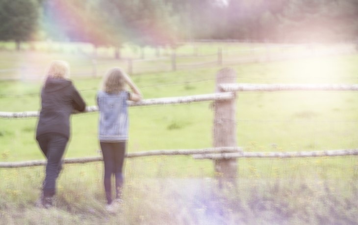 Mother and daughter talking, leaning against a fence