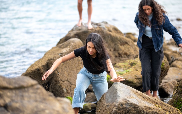 Teenagers climb on rocks by the ocean