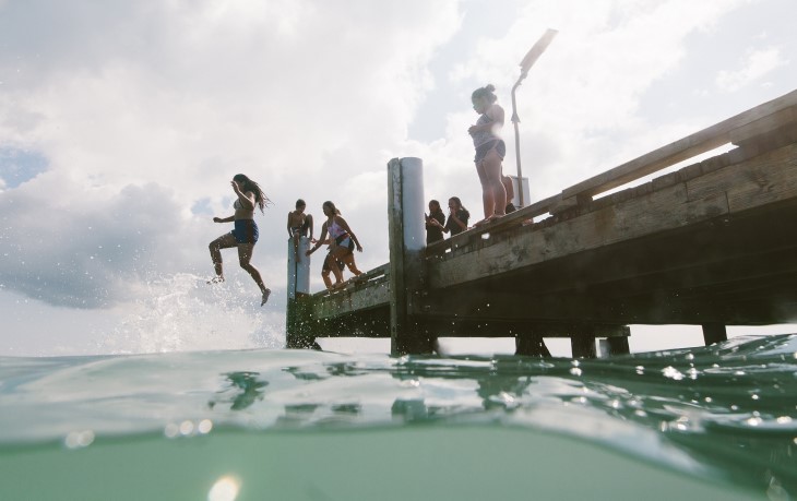 A group of teenagers jumping off a pier into the water.