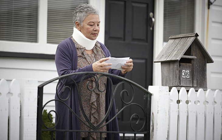 Woman with neck brace reads letter at letterbox