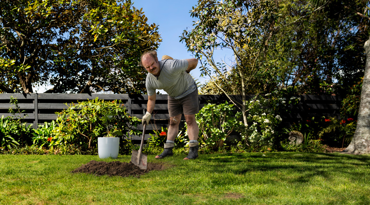 person bending over with a spade in the garden holding his back