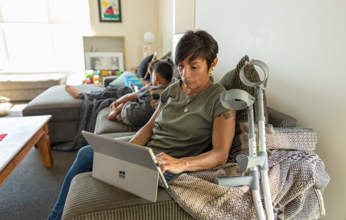 Woman working on laptop sitting on couch with crutches