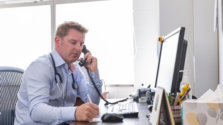 Health provider talking on the phone sitting at desk making notes on paper