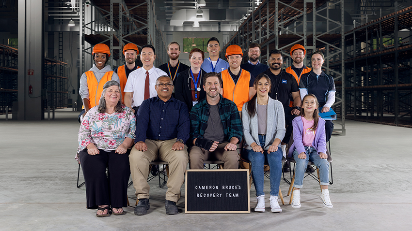 Recovery at work extended team of injured worker, whanau, colleagues, health providers and ACC posing for bleachers-style photo in warehouse