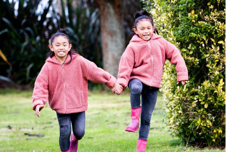 Two young girls run through the backyard holding hands in their pink jumpers