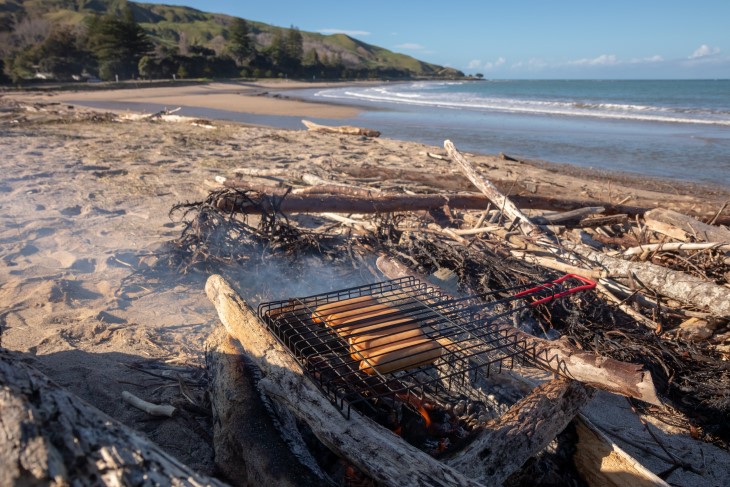 Sausages grilling on an open fire on a beach. 