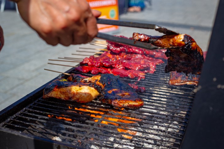 A close-up of a man's hand using tongs to turn meat on a BBQ. 