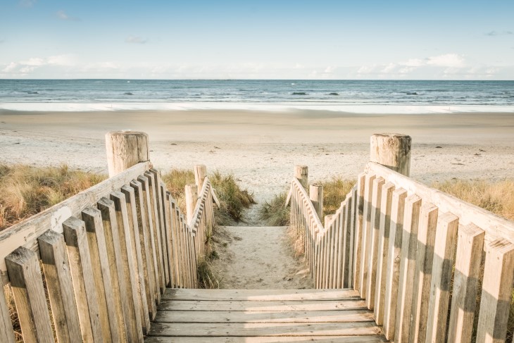 Camera looks down wooden walkway towards sandy beach