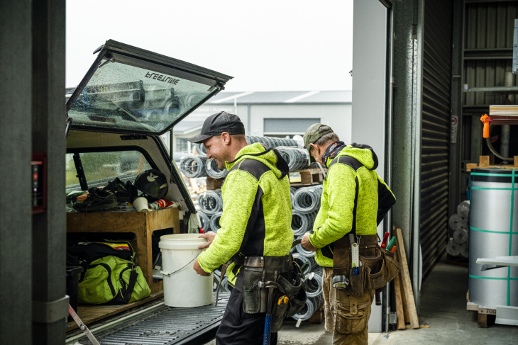 A pair of construction workers loading materials into the back of a vehicle.