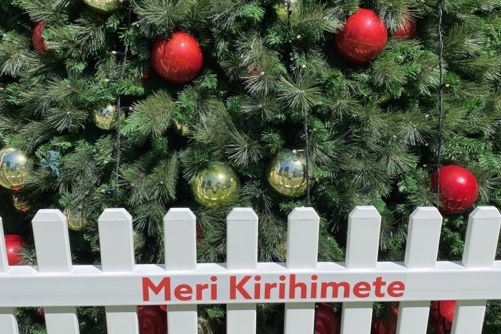Close up of a tree with a picket fence reading Meri Kirihimete next to it
