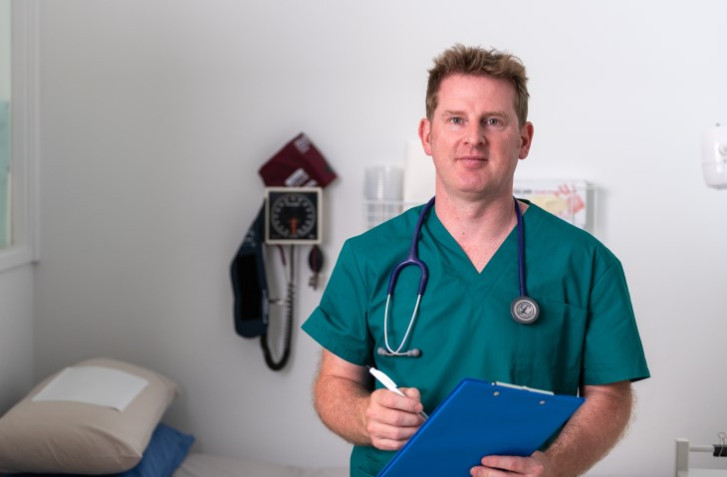 Doctor in green scrubs holds a blue clipboard