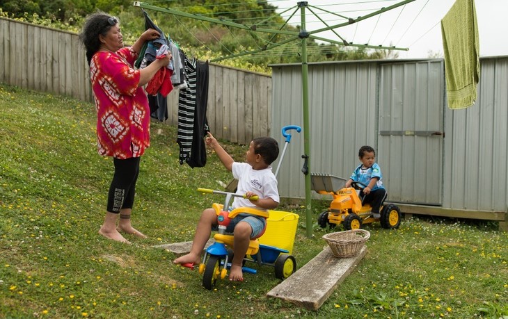 Grandmother hanging washing outside with children playing Grandmother hanging washing with grandkids on ride-on toys