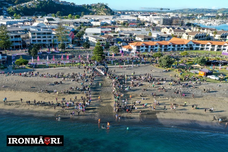 An aerial photo of the IronMāori finish line, showing competitors and spectators on the beach. 