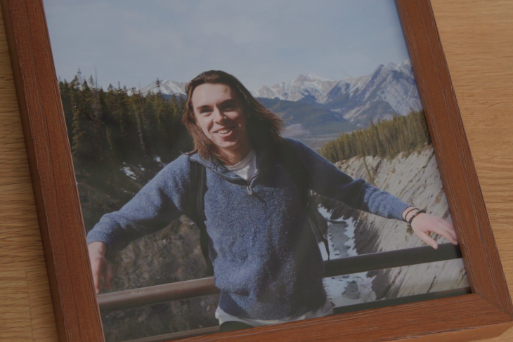 A smiling image of Jack Skellett standing on a bridge with mountains in the background