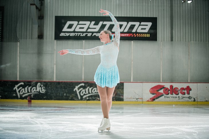 Lydia does a ballet pose on her ice skates, with her left arm up above her head