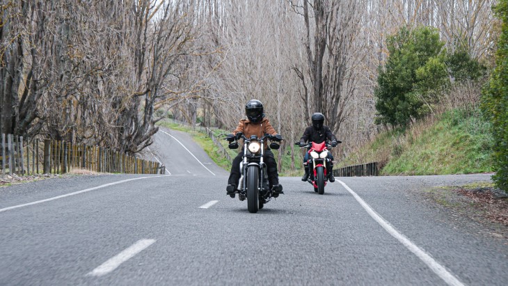 Mandy and her hsuband ride their motorbikes down a road with trees in the background