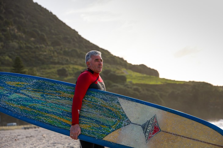 Michael Dixon holds his surfboard on the beach in Tauranga