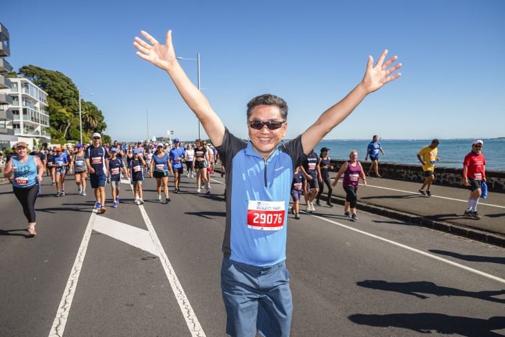 Round The Bays participant throws their arms in the air as they pass the line