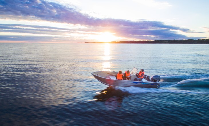 A boat motoring along on the water with several people on board.