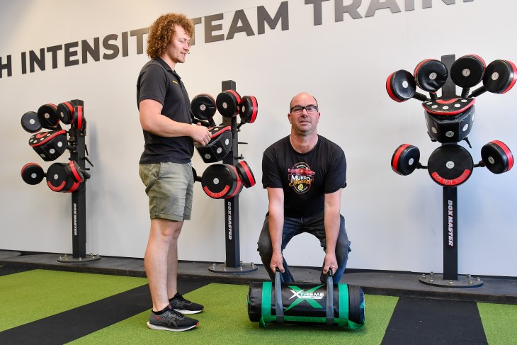 Adrian Reid lifting a weight in the gym while his physio supervises.