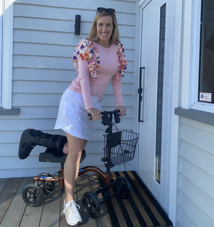 Alicia Mabey kneeling on a knee scooter and smiling.