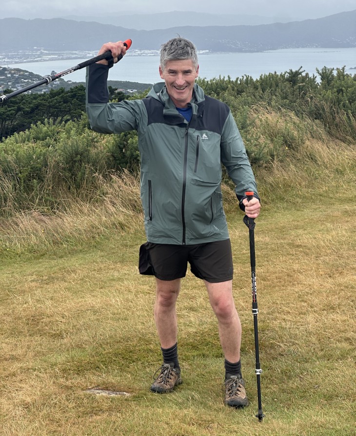 Andrew Leslie standing on the top of Mt Kaukau holding his walking sticks and smiling.