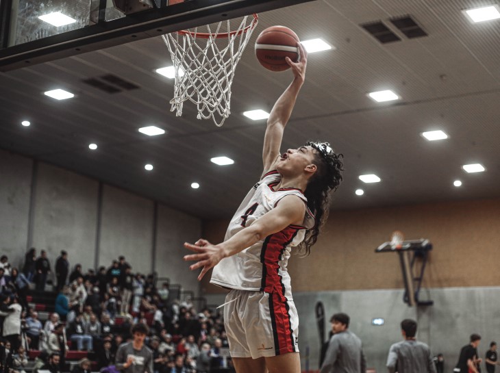 A young man slam dunks the ball into a basketball hoop. 